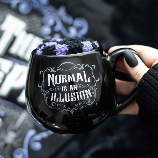 Indulge your spooky side with this Normal Is An Illusion Mug &amp; Sock Set. The black rounded mug features the phrase Normal Is An Illusion in striking white letters, while the pair of fluffy purple and black stripped socks adds a touch of whimsy to your wardrobe. Embrace your gothic style with this unique homeware and accessory set