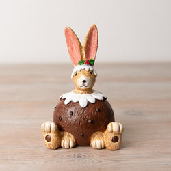 Christmas Pudding Bunny Sitting. A fantastically characterful bunny sitting down on its bottom with four paws facing front while wearing a Christmas pudding with icing and a sprig of holly on its head, making a great edition to your festive decoration, Christmas tier tray or a gift for a friend