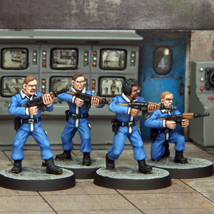 Minion with Rifles by Crooked Dice, a set of four 28mm scale metal miniatures depicting henchmen wearing matching blue uniforms and black boots, with all four holding rifles and one down on one knee. 