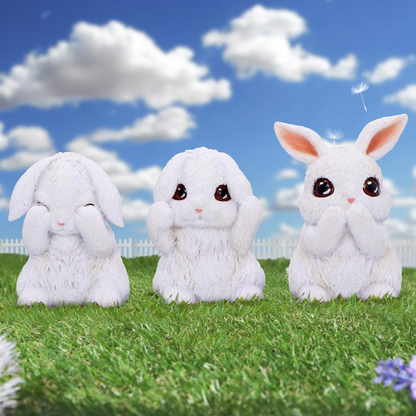 Three Wise Bunnies in the iconic See No Evil, Hear No Evil, Speak No Evil poses. white rabbit figurines on a cute grass, blue sky and white cloud background. 