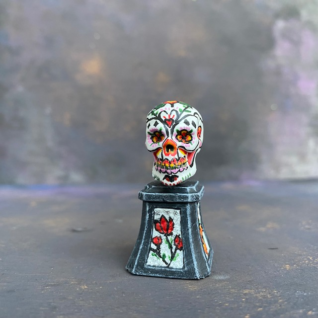 Prepainted Sugar Skull from the Reaper Miniatures bones USA range hand painted by Mrs MLG, a brightly coloured skull on a plinth. 