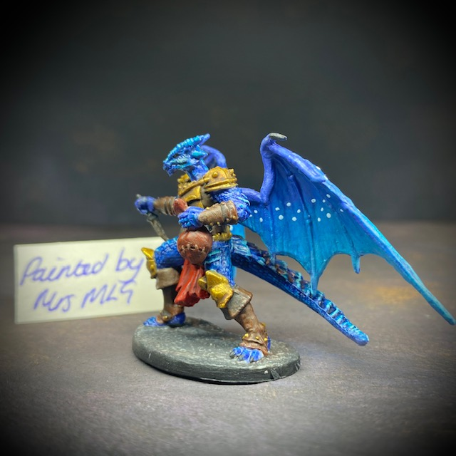  dragonfolk rouge holding a dagger in one hand and a pouch in the other. Mrs MLG has painted this miniature with a blue palette adding white dot effects to the wings, the armour is golden colour and Tazythas has a red loin cloth.