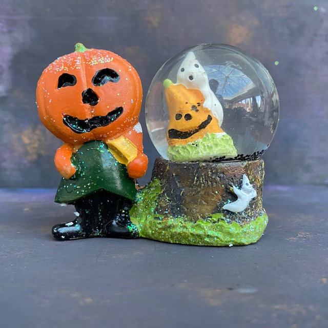 this ornament features a pumpkin holding an candy corn in one hand, she is next to a globe which has black 'snow' and a pumpkin and ghost. Spooky snowglobe Halloween decoration