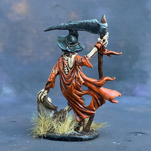 Gauntfield by Reaper Miniatures from their Bones range pre painted by Mrs MLG.  A bones miniature of a skeleton scarecrow holding a scythe in one hand and a bag of bones in the other, pre painted with orange and blue colours.