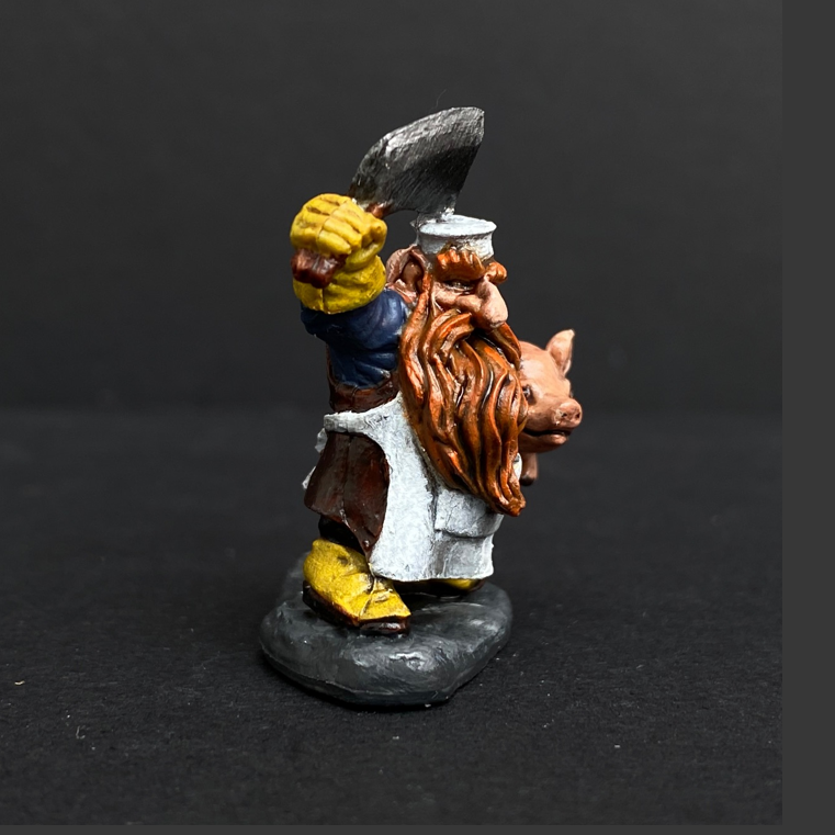 Hand painted dwarf butcher from the Reaper Miniatures range. Mrs MLG has painted this dwarf butcher with a yellow, blue and white colour scheme with a vibrant beard holding a clever above his head and a cute pig under his arm. 