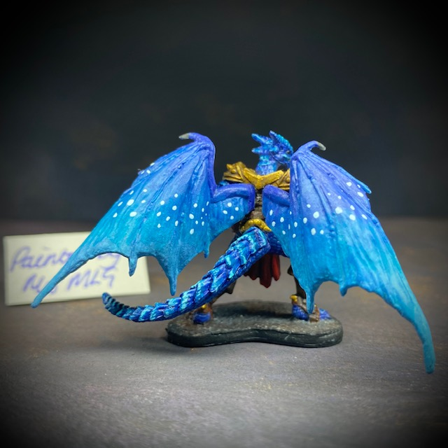  dragonfolk rouge holding a dagger in one hand and a pouch in the other. Mrs MLG has painted this miniature with a blue palette adding white dot effects to the wings, the armour is golden colour and Tazythas has a red loin cloth.