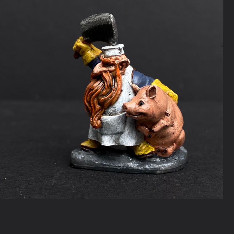 Hand painted dwarf butcher from the Reaper Miniatures range. Mrs MLG has painted this dwarf butcher with a yellow, blue and white colour scheme with a vibrant beard holding a clever above his head and a cute pig under his arm. 