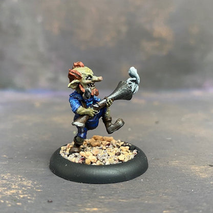 Boom Boom McBoom from the Moonstone mushroom and mayhem troupe box,  pre painted by Mrs MLG. This wonderfully sculpted miniature is of a Goblin holding a rather large smoking gun, with a pipe in his mouth and wonderful grin on his face. This delicate miniature is painted with greens, blues and browns. 